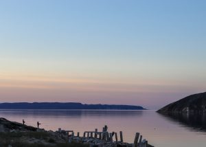 Photograph of a lake at sunrise, with the silhouettes of two people fishing in the bottom left corner.