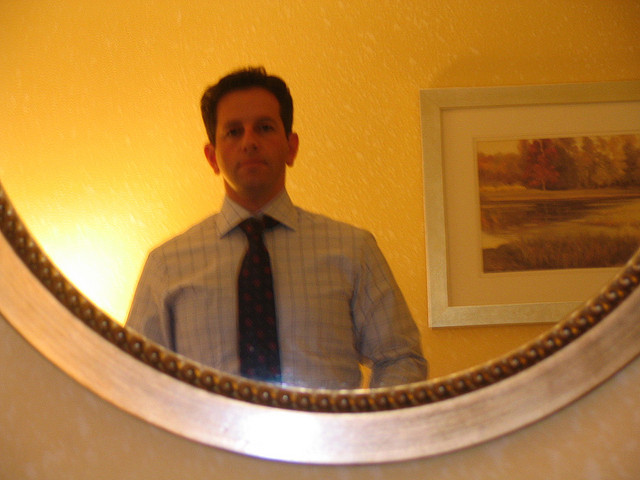 A man trying looking in a mirror while trying on a suit before his interview